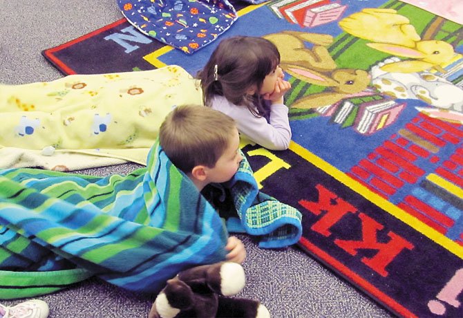 Alex Jones, 3, and friend Sarah Mace, 4, of Springfield, snuggle in their blankets to listen to librarian Twyla Turner read winter-themed books during Twilight Tales at Kings Park Library in Burke Tuesday, Jan. 24.