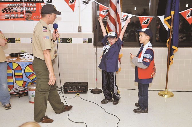 Cubmaster and Pinewood Derby emcee Andrew Gallotta awards Best Design medals to Bear Scouts Aidan DeVore, with arms raised in celebration, and Jackson Tomasco at Pack 1965’s Pinewood Derby.