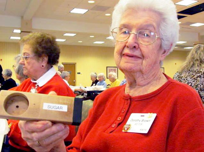 Dot Brown, one of Greenspring’s volunteers, holds up a measuring cup for sugar made by residents in Greenspring's woodshop. 