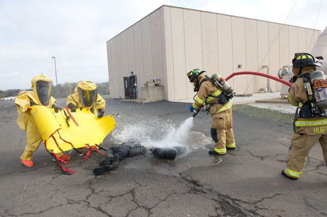 In this training scenario, the wrong chemicals have been added to a storage tank at this facility, injuring two people.  Firefighters in the Hazmat suits (on left) have just moved the two victims from the contaminated building in the rear to a decontamination area where the victims are decontaminated by other members of the Hazmat team.
