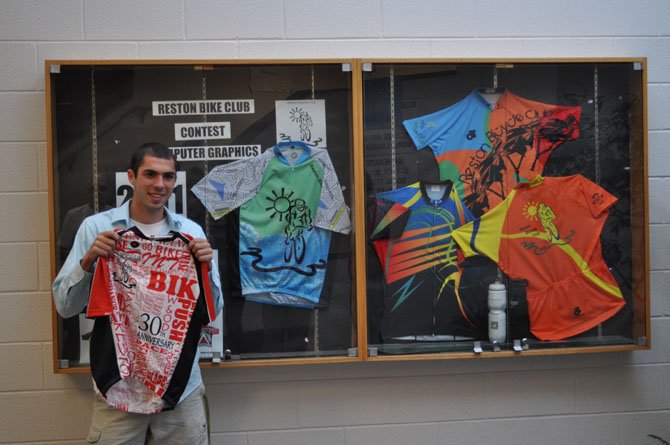 Tyler Hutchins holding up the jersey in front of the case showcasing the last four years' winning jerseys.