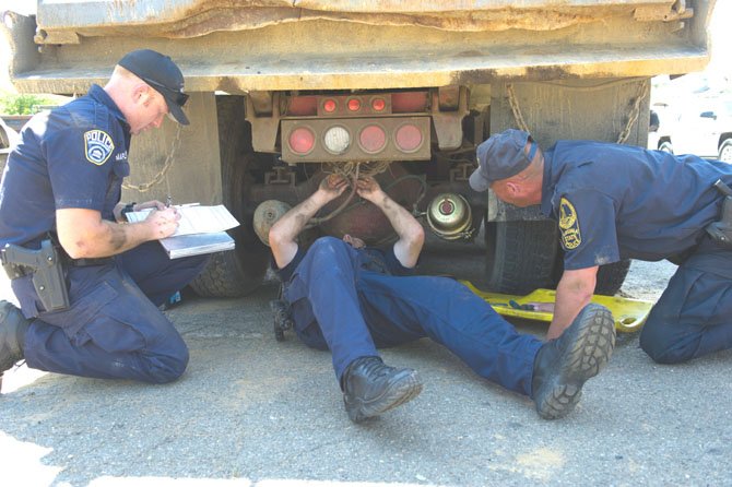 Officer Ben Maplethorpe (left) and his colleague Officer Mik Laird of the Arlington Police Department work with Virginia State Trooper John Wolford at a joint vehicle inspection effort at E. C. Lawrence Park involving nine local law enforcement agencies on May 31.  During the effort, 110 trucks were inspected, 288 infractions were found putting 40 out of service.