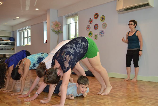 Instructor Linda Feldman leads a group of yoga campers in a downward dog tunnel at Budding Yogis. Specialty camps could be an option for parents still searching for summer activities for their children.

