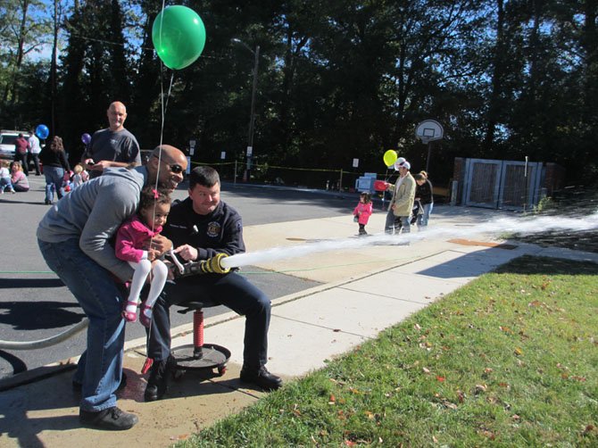 Chloe Edmondson, with a bit of help from her father and a firefighter, aims a powerful spray of water at a target.