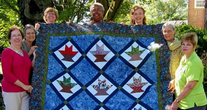 Quilters hold up their 2012 quilt, "Baskets of Joy," which will be raffled at the MVUC Holiday Shop Saturday, Nov 17.
