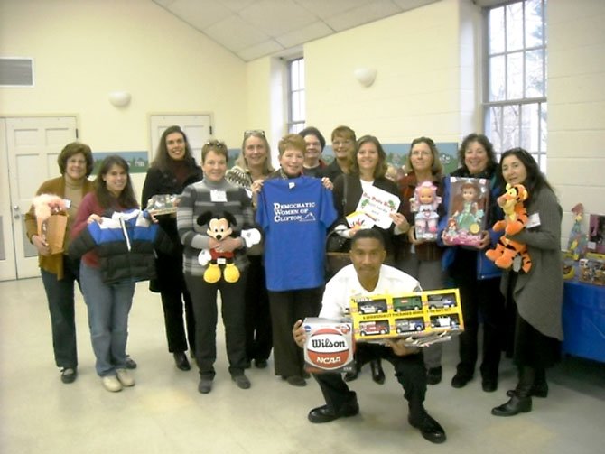 At its Nov. 18 general meeting, the Democratic Women of Clifton members collected toys, gift cards to Target, Old Navy and grocery stores, and donations to purchase winter coats for children. Members of the DWC gather around Captain Will Bailey of the Fairfax County Fire and Rescue Department (front), who holds a donated basketball and toy trucks. Lisa Whetzel, executive director of Our Daily Bread, stands directly behind him. 