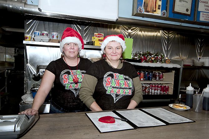 Wait staff and cooks, from left, Barbara “Barbie” Gollick and Angie Brosen, display one of the several holiday t-shirts for the 29 Diner and their Santa hats. 