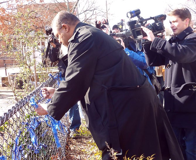 Alexandria Police Chief Earl Cook ties a blue ribbon to the fence at Lyles-Crouch Traditional Academy March 22 near where Officer Peter Laboy was shot.