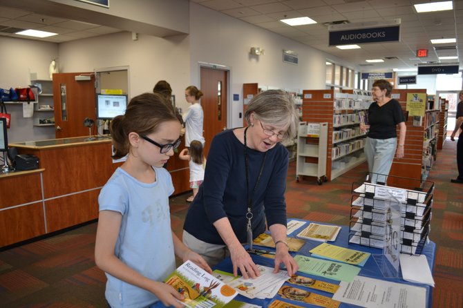 Richard Byrd Library Branch Manager Sally Eckard shows a young reader information about the summer reading program.