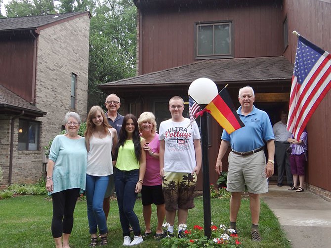 From left, Elaine Montgomery, Olivia Kühne, Alan Montgomery, Özge Kayalar, Becky Biondi, Dominick Zeitz and Dan Biondi pose with the American and German flags outside the Montgomery’s home in Reston.