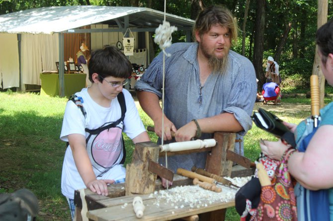 Acting as an apprentice, Riley Soos, 11, works with an artisan to spin cotton into thread.