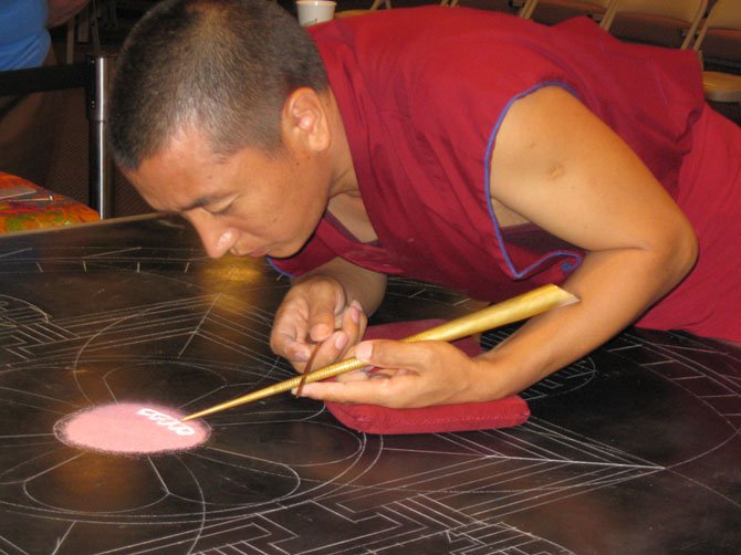 A Tibetan monk uses a chakphur or metal funnel to build the mandala sand painting on the template.