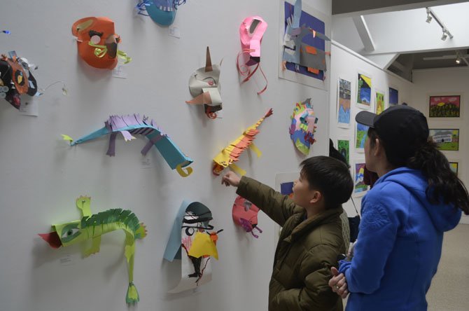 Youth art exhibition visitors admire a wall lined with colorful paper figures.