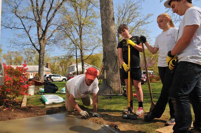 Beck Moniz, Kate and Emma Sapp listen and watch as a volunteer smooths out a freshly poured concrete slab.
