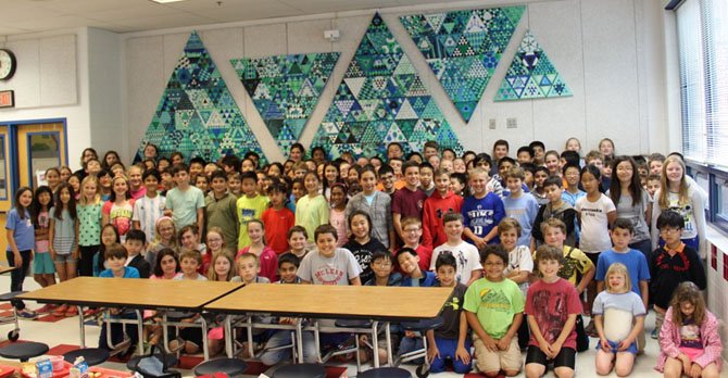 The entire Churchill Road fifth grade class poses in front of the triangular wall art they created for the school’s cafeteria.