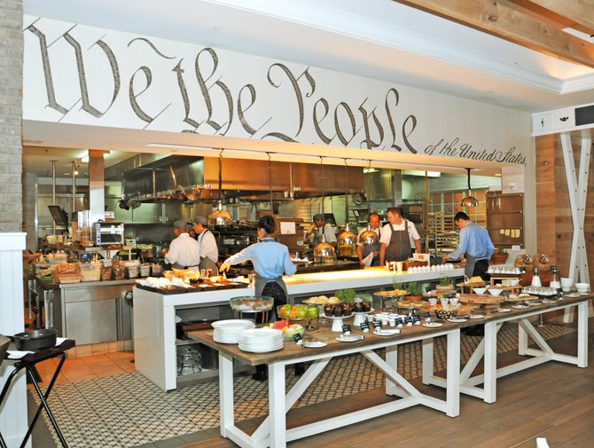 The main dining hall includes a direct view of the bright, open kitchen where diners can view the chefs at work. Framing the kitchen is a bold excerpt from the U.S. Constitution.