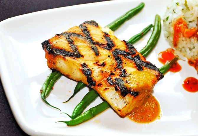 A salmon steak sits atop a bed of healthy green beans. The other two fish steaks included in this dish are tuna and sea bass. Fish items are available seasonally.