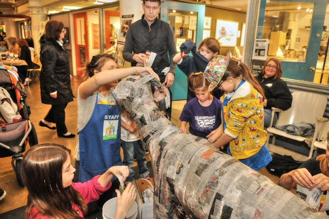 As more children arrive, the life-size papier-mâché dog begins to get a coat of newsprint. The papier-mâché sculpture was organized and created by Torpedo Factory artist Lisa Schumaier and Kelly Organek of UpCycle. 