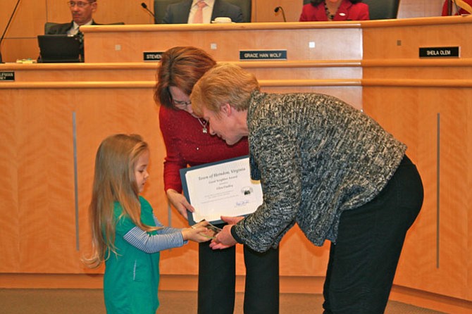 Martha Durden, 3, hands the Good Neighbor award to Ellen Findley with the aid of Mayor Lisa Merkel.
