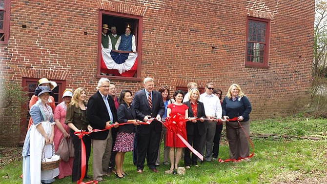 Park staff, volunteers and community leaders hold the ceremonial ribbon for the restoration celebration of Colvin Run Mill historic site.