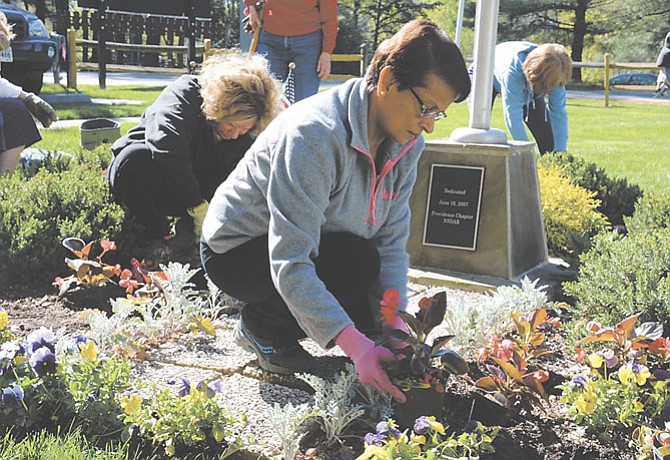Dominion Valley Garden Club members and Fairfax Station residents Carole Burk (left) and Bharti Amin (right) swap purple and yellow pansies for more patriotic red begonias at the Fairfax Station Blue Star Memorial garden.