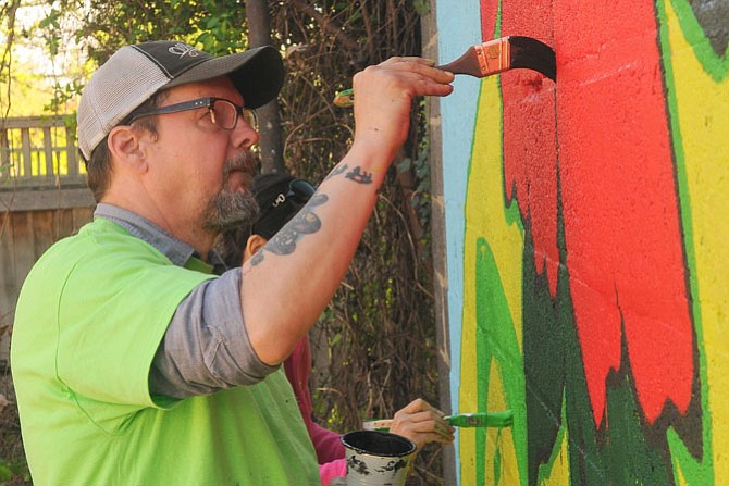 Artist Chad Brady works on a mural he designed on a brick and cinderblock wall behind on of The Salvation Army temporary residences on Mt. Vernon Avenue.
