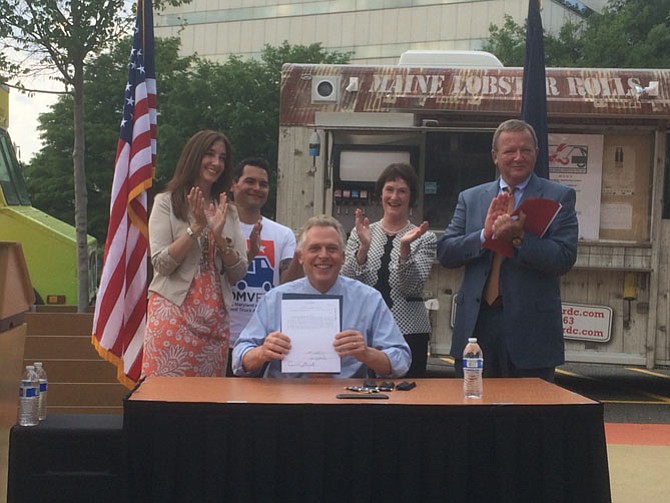 Rear from left, Del. Eileen Filler-Corn (D-41), Board of Supervisors chairman Sharon Bulova, Executive Director of the DMV Food Truck Association Che Ruddell-Tabisola and Jim Corcoran, President & CEO of the Fairfax County Chamber of Commerce applaud as Gov. Terry McAuliffe (D) signs a bill calling for regulations for food trucks to operate on specific roads in Virginia.