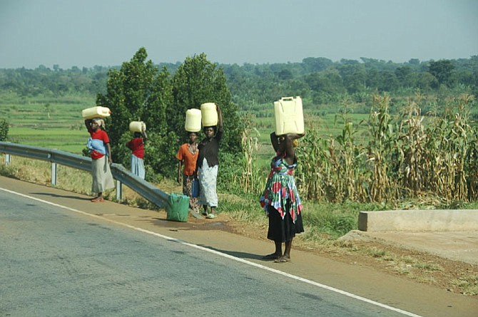 Women and children in Uganda carry heavy water jugs back to their villages.