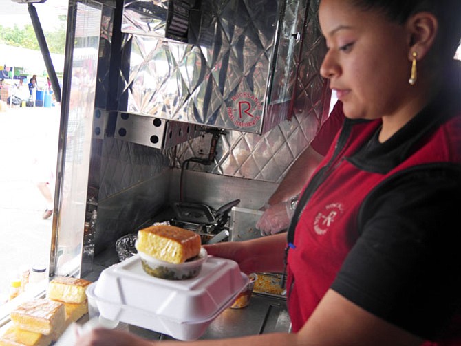 Claudia Cruz, Rocklands Barbecue food truck coordinator, hands over an order of baby-back ribs with a container of collard greens and a chunk of cornbread to a customer waiting outside the window of the food truck.
