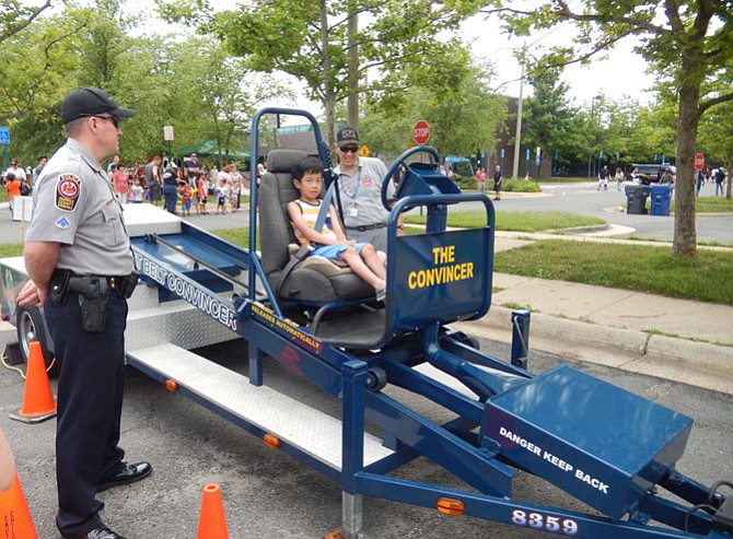 Trying out the police seatbelt convincer is George Tunaya, 7, as MPO Patrick Nolan Jr. (on left) looks on.
