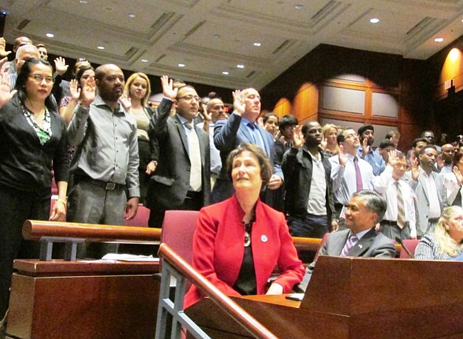 New Americans take an oath of allegiance at a naturalization ceremony held at the Fairfax County Government center June 12. (Front) Board of Supervisors chairman Sharon Bulova (left) and Ret. Maj. Gen. Antonio Taguba (right), born in the Philippines, observe the ceremony.