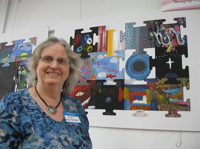 Artist Shari MacFarlane stands in front of the Healing Wall Puzzle painted by soldiers who suffer from PTSD.
