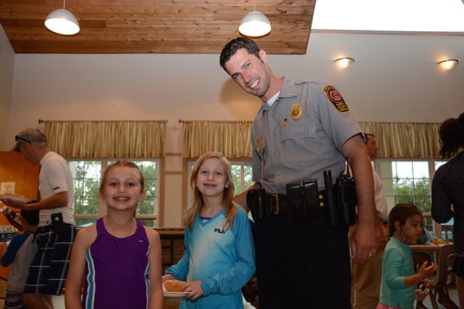 (From left) Katelyn and Elizabeth Stuebner meet with Lt. Eli Cory, assistant commander of the West Springfield district police station, before adding condiments to their hot dogs during National Night Out in Little Rocky Run.
