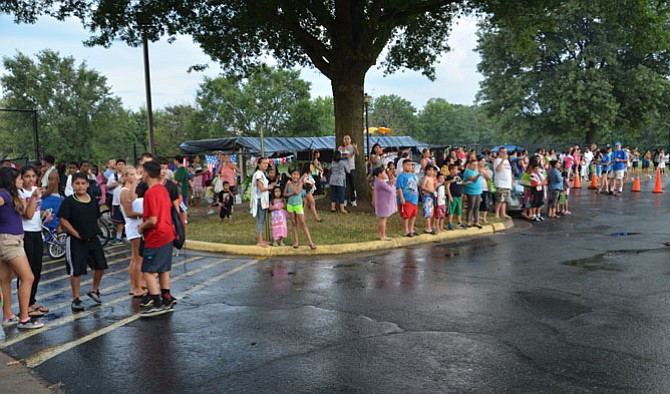 The crowds await the arrival of the motorcade bringing Herndon law enforcement personnel, town officials and volunteers to the last stop on the National Night Out 2015 route. The wait – and the rain drenching – were worth it, as the gathered neighbors were treated to goodies, a motorcycle handling performance and the arrival of a Fairfax County police helicopter for an up-close inspection.
