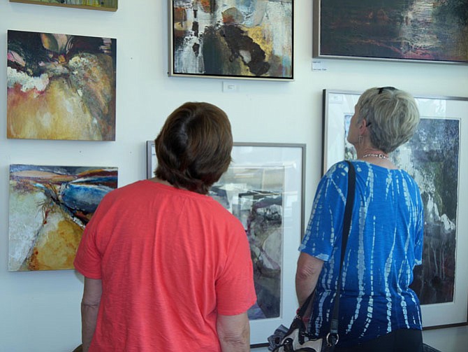 Two people walk through the studio observing the paintings on the wall and having a conversation about what they see and which they like the best.
