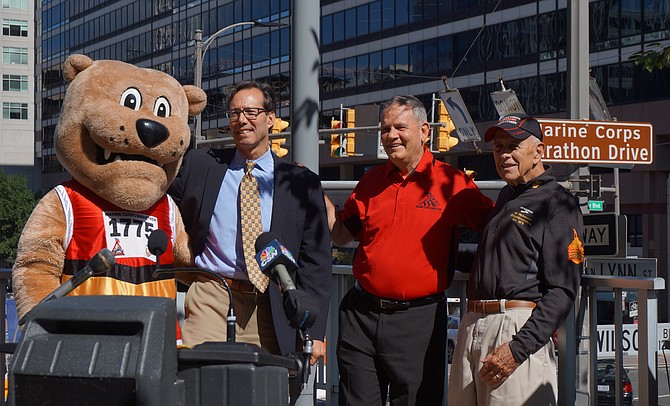 Arlington County Board member Jay Fisette, second from left, is joined by Marine Corps Marathon mascot Miles the Bulldog, MCM race director Rick Nealis and Al Richmond at the unveiling of Marine Corps Marathon Drive Oct. 7 in Rosslyn. The sign at the corner of N. Lynn St. and Wilson Blvd. will be hung every October in honor of the marathon, which begins and ends in Arlington.
