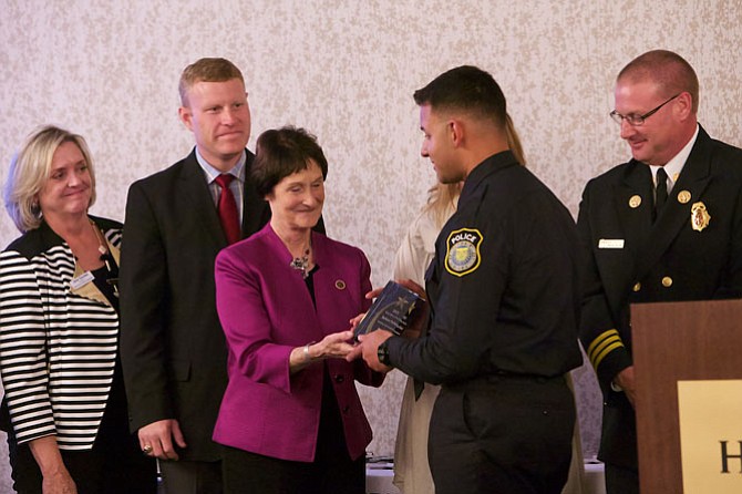 Fairfax Board of Supervisors Chairman Sharon Bulova smiles as she hands the Police Officer of the Year award to Officer Jackson Parker. Parker, of the Fort Belvoir Department of Public Safety, responded to a call from a mother who reported her son was locked in a bedroom, with a knife. He used his training to talk to the youth, diffuse the situation, and get the teen transported to a hospital where he could receive help. 
