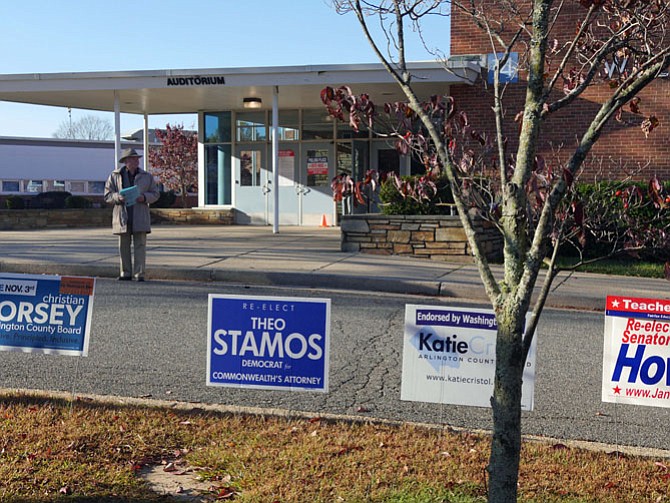 Signs line the curb for local candidates at Williamsburg Middle School polling place as a volunteer holds information for potential voters.
