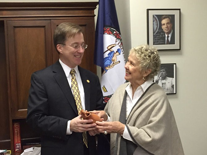 State Del. Paul Krizek shows off clay pot from the Pamunkey Indian reservation to Kay Smith. A photo of Olympian Billy Mills, the first American and American Indian to win the 10,000 meters, hangs in the background. 
