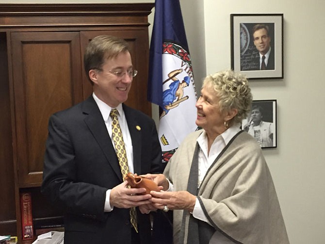 State Del. Paul Krizek shows off clay pot from the Pamunkey Indian reservation to Kay Smith. A photo of Olympian Billy Mills, the first American and American Indian to win the 10,000 meters, hangs in the background. 
