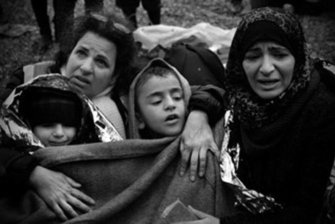 Kathy Hertz (left) of Clifton sits with a refugee mother and children as they get warm after arriving on the Greek shore by dinghy.