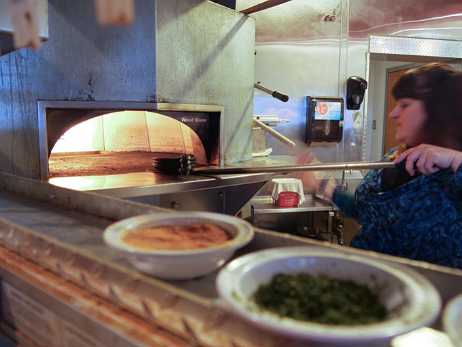 Marylisa Lichens pulls a pizza from the 630 degree oven at Fireflies. The restaurant began as a pizza place 13 years ago but the favorite “hands down” is currently the burger, enjoyed by President Obama a couple of years ago. 
