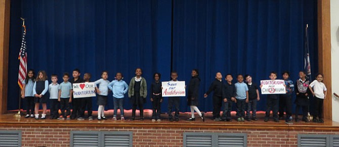 Students on the stage at Patrick Henry Elementary School with signs about plans for a cafetorium.
