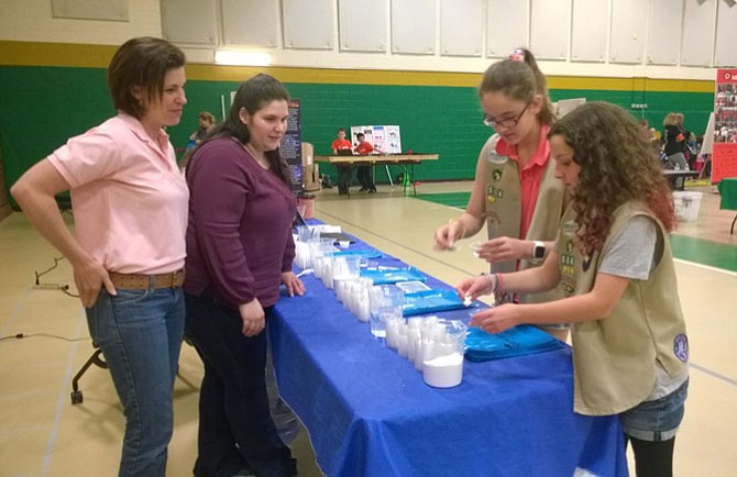 From left -- Leaders Mary Nelson and Jessica Druetto of Troop 4914 in Burke-Springfield show 12-year-old Girl Scouts Annabelle Perry and Sarah Turner of Troop 2652 in Loudoun County how to “make snow” by using water to change the physical state of a sodium carbonate polymer.   
 
