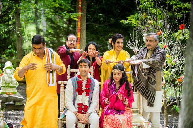 Pandit Shri Tripathiji of the Rajdhani Mandir in Chantilly (left) presiding over a ritual puja welcoming Riddhima (seated, right) to the Mehta family home after her marriage to Neil (seated, left), with the blessings of their parents (standing from left, Dinesh Mehta, Raksha Mehta, Shabnam Gandhi and Guarang Gandhi. The puja was performed on  May 15 at the Mehta residence in Great Falls.

