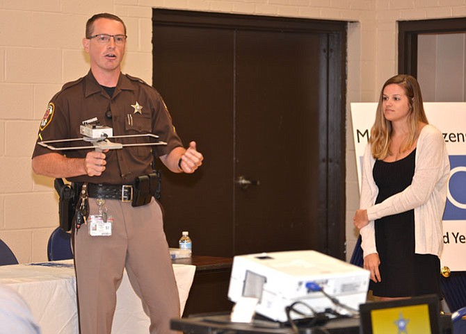 With the assistance of audience member Kaylen Rice as volunteer, Second Lieutenant Stacie Talbot with the Fairfax County Sheriff’s Office demonstrates the device used to track missing “at-risk” citizens like those with dementia. “Project Lifesaver” is fairly new, but already has 100 active clients. The program is free to those who qualify, but since it depends on private support to help fund the purchase of the trackers, there is a wait list for new clients. Contact Stacie.Talbot@fairfaxcounty.gov for more information.
