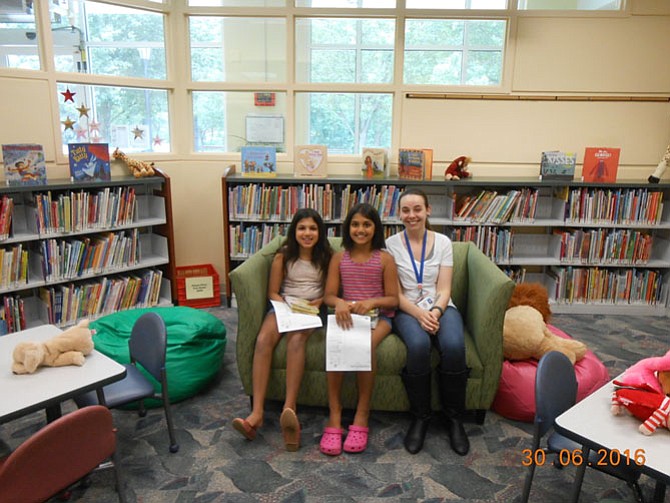 Nishka and Aanya in the children's reading area in the Great Falls Library with a librarian.

