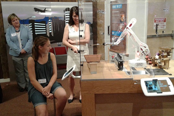 Amy Burke, board chair of the Children's Science Center Lab, and executive director Adalene “Nene” Spivey watch Emily Brunner, 15, of Falls Church take on the robotic arm challenge after programming the device to play the “Happy Birthday” song on a xylophone following a Sunday morning ribbon cutting in Fair Oaks Mall. Brunner participated on her school’s robotics team at George C. Marshall High School. 

