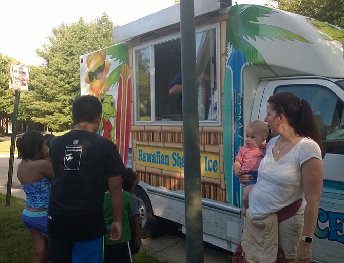 Anne Marie McCaskin, 37, holds her 24-month-old son, Toby, and watches their young neighbors line up for free shaved ice at a  National Night Out block party held Aug. 2 in the Random Hills townhouse community near Fairfax Corner.  She appreciates her local law enforcement agency and doesn’t want her kids to be afraid to ask for help from police officers when they need it.
