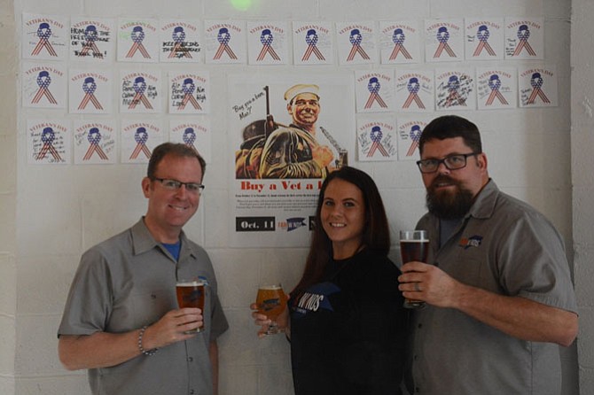 From left, Fair Winds Brewing Company CEO Casey Jones, tasting room manager Jacquelyn Olejniczak and brand ambassador Mike Kuykendall in front of the brewery wall holding ‘Buy a Vet a Beer’ notes.